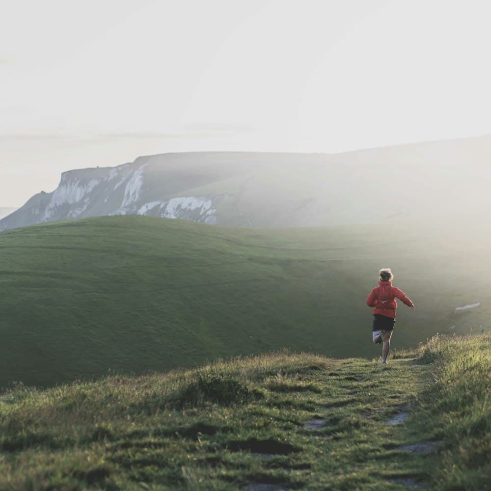 A person running along a grassy hillside trail in morning light